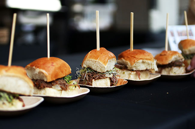 Pulled pork sliders in a line on a black table.