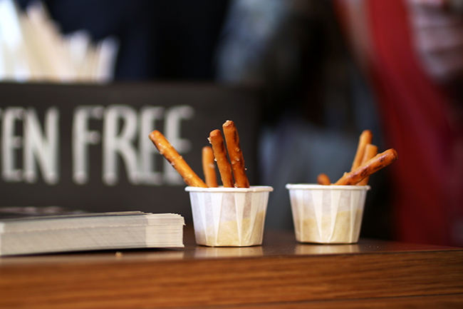 Two small paper cups filled with mustard and pretzel sticks.