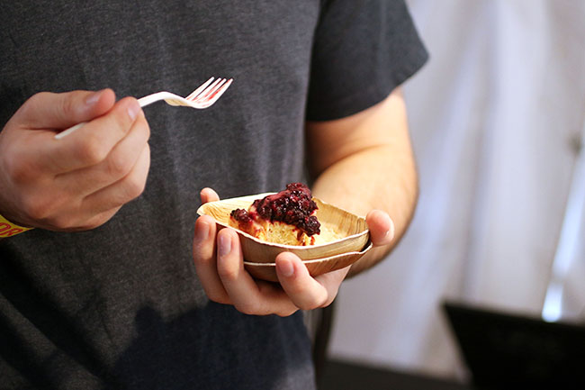 Man in a grey shirt holding a wooden plate with a cinnamon bun and fruit compote.