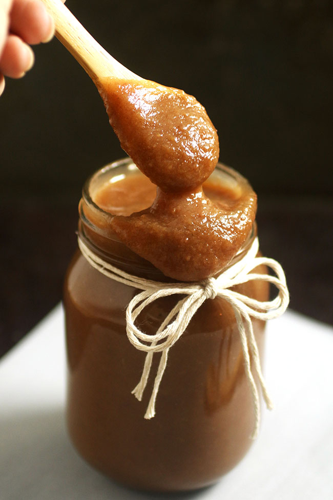 Wooden spoon pouring apple butter into a mason jar.