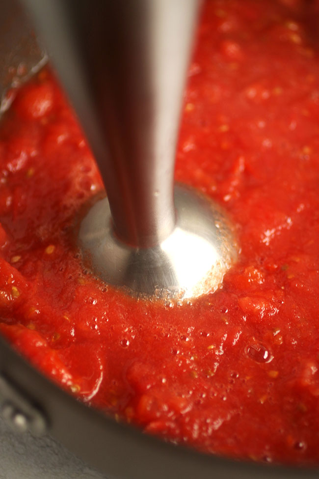 Hand blender in a pot of tomato sauce.