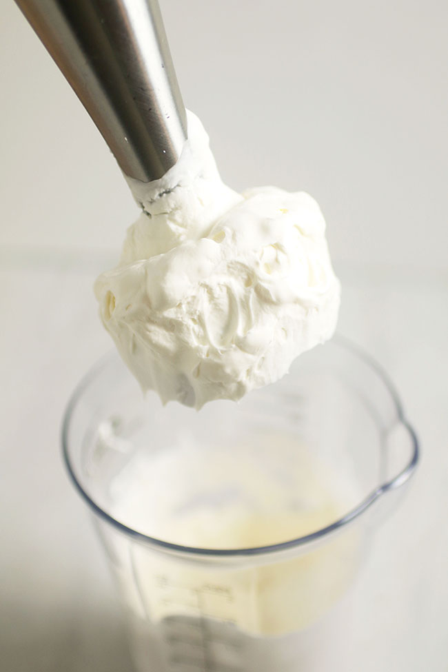 Immersion blender lifting whipped cream out of a jar.