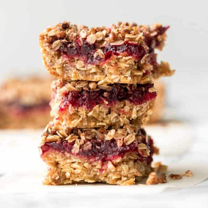 Three cranberry oat bars in a stack on a white table.