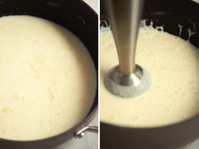 Immersion blender blending cheese sauce in a dark pot.