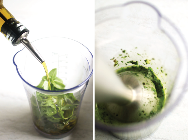 Immersion blender blending basil and olive oil into pesto in the plastic beaker.