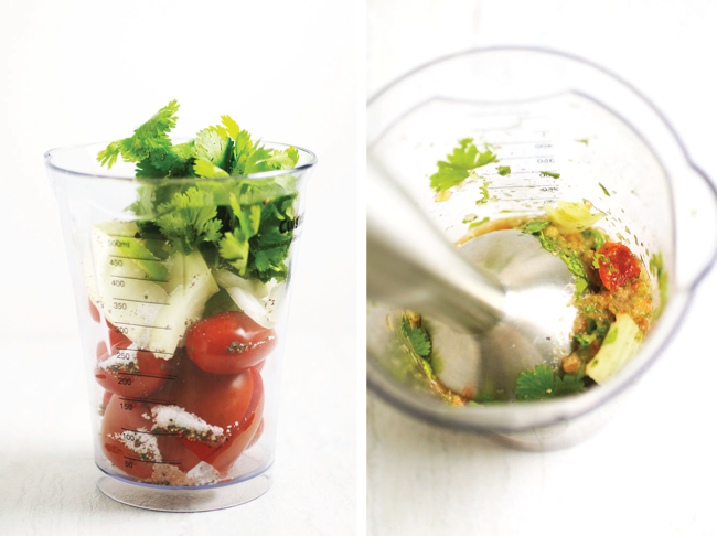 Tomatoes, onion, and fresh cilantro in a beaker with an immersion blender.