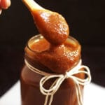 Wooden spoon lifting apple butter out of a glass jar.