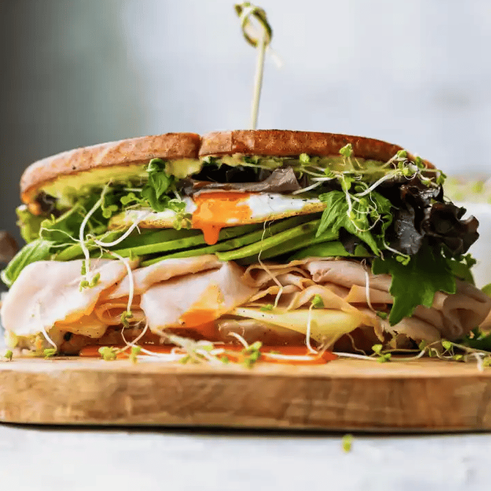 Turkey and avocado sandwich with a fried egg on a white table.