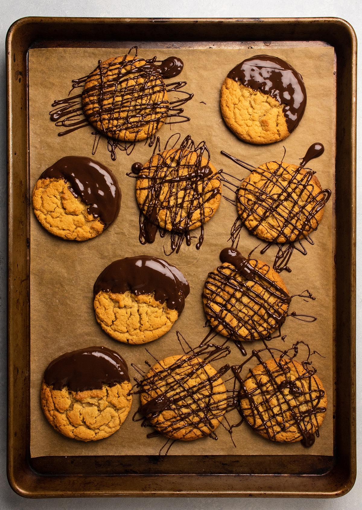 Peanut butter cookies covered in melted chocolate on a large baking sheet.