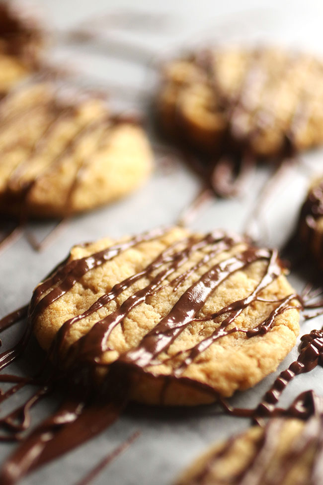 Peanut butter cookie drizzled with melted chocolate on a piece of parchment paper.