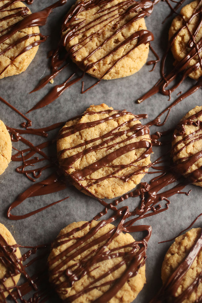 Nine peanut butter cookies drizzled with melted chocolate on a piece of parchment paper.