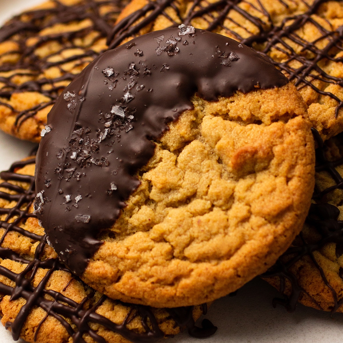 Chocolate dipped peanut butter cookie on top of several cookies drizzled with chocolate.
