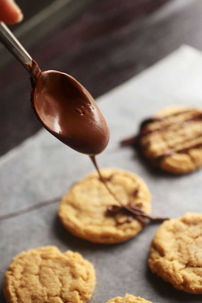 Spoon drizzling melted chocolate over a pan of peanut butter cookies.