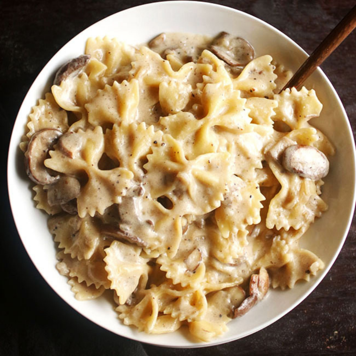 Bowtie pasta with creamy mushroom pasta sauce in a shallow white bowl on a brown background.