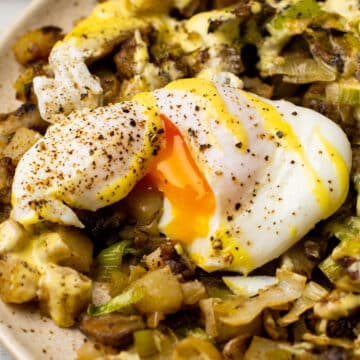 Poached egg on leek and mushroom hash with yolk running out.