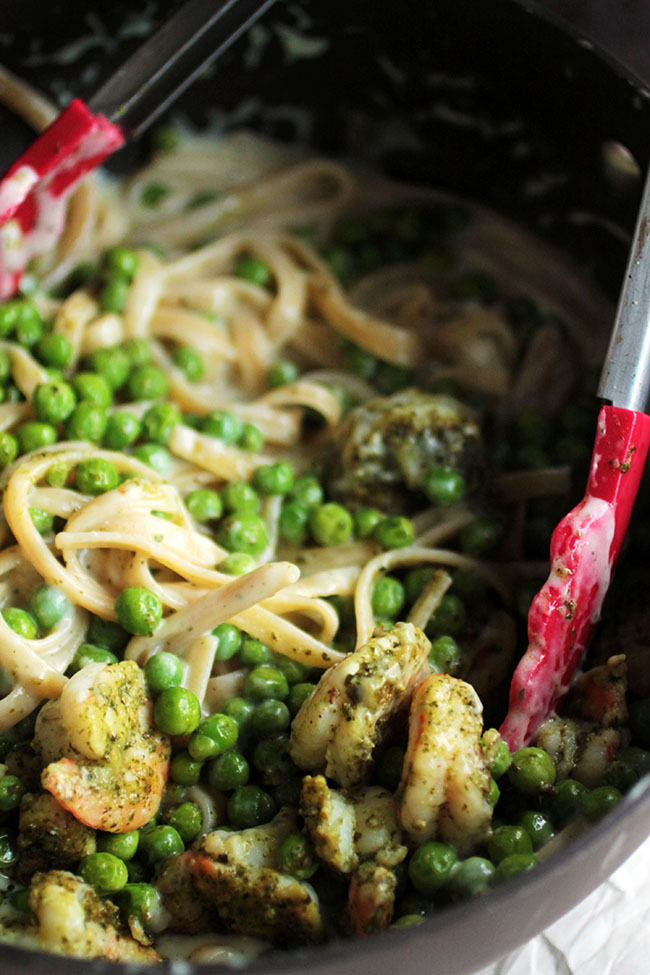 Shrimp fettuccine alfredo with peas in a large pot being tossed by red tongs.