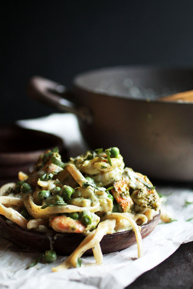 Shrimp fettuccine on a wooden plate topped with fresh peas and chopped basil.