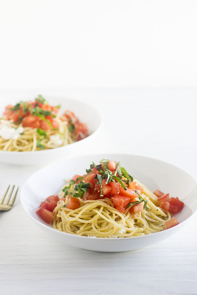 Two white bowls of caprese pasta on a white background.