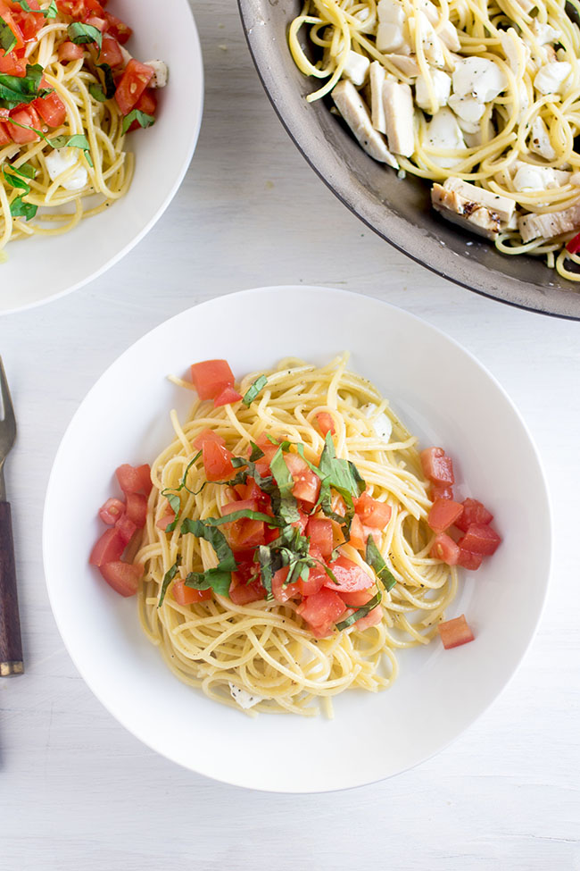 Spaghetti in a white bowl topped with chopped tomatoes and fresh basil.