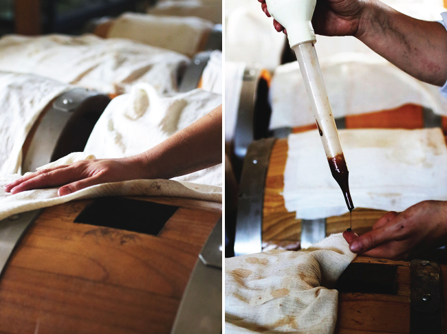 Hands using a baster to pull a sample of balsamic vinegar out of a barrel.