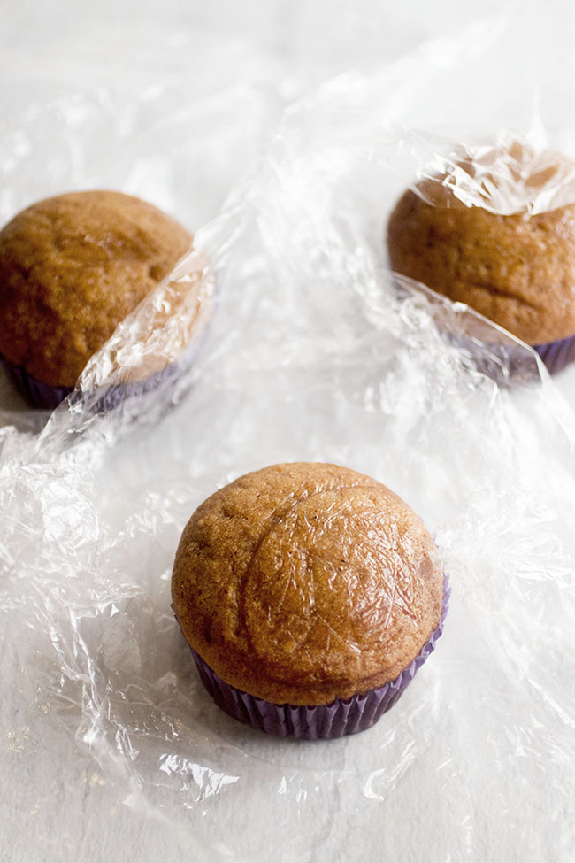 Unfrosted pumpkin cupcakes sitting on squares of plastic wrap.