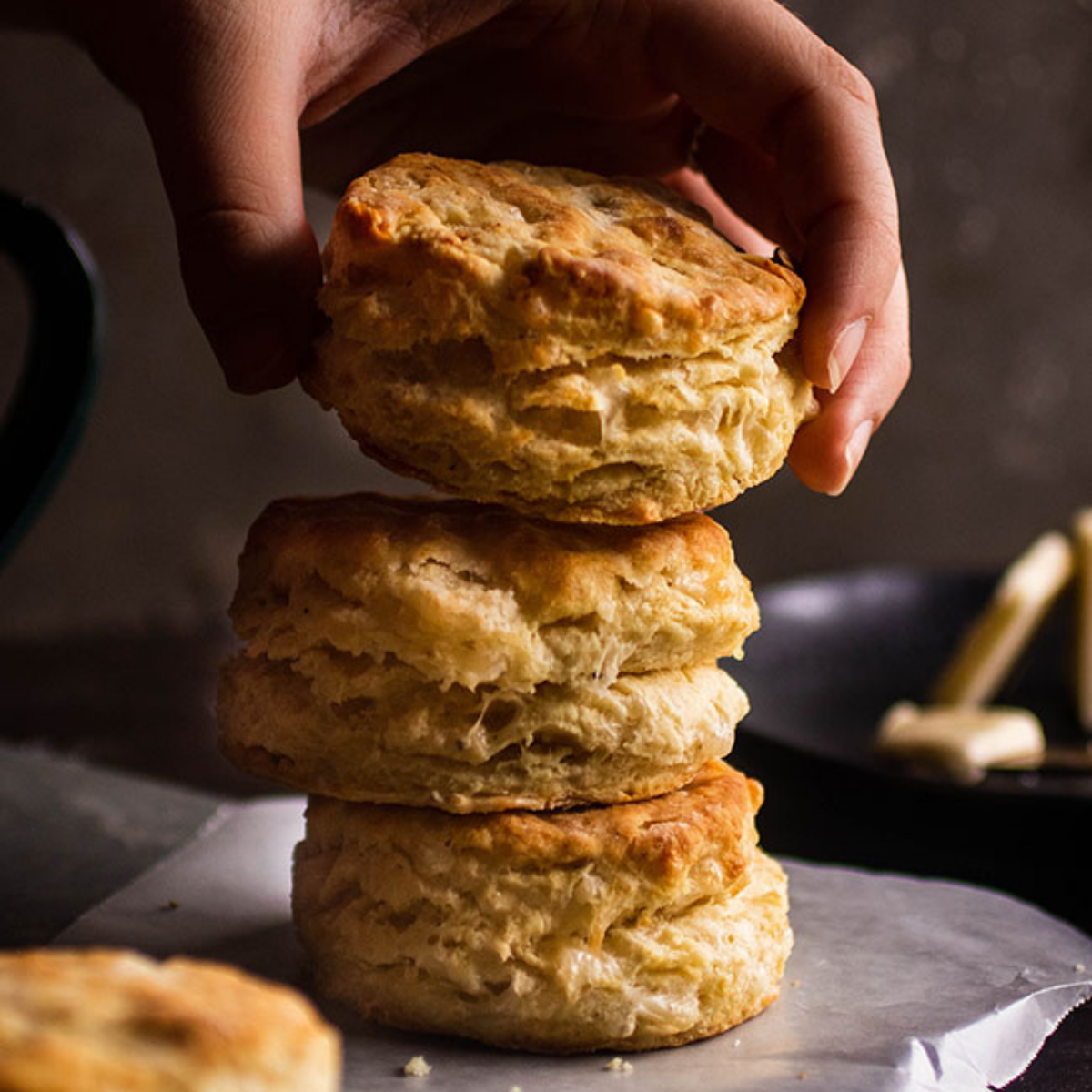 Woman's hand adding a gruyere biscuit to a stack of biscuits.