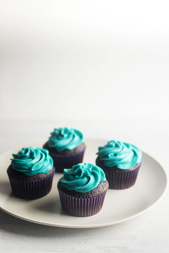 Four cupcakes with blue frosting on a white plate.