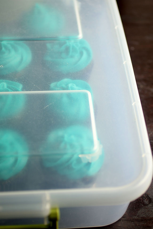 Cupcakes with blue frosting in a plastic storage container.
