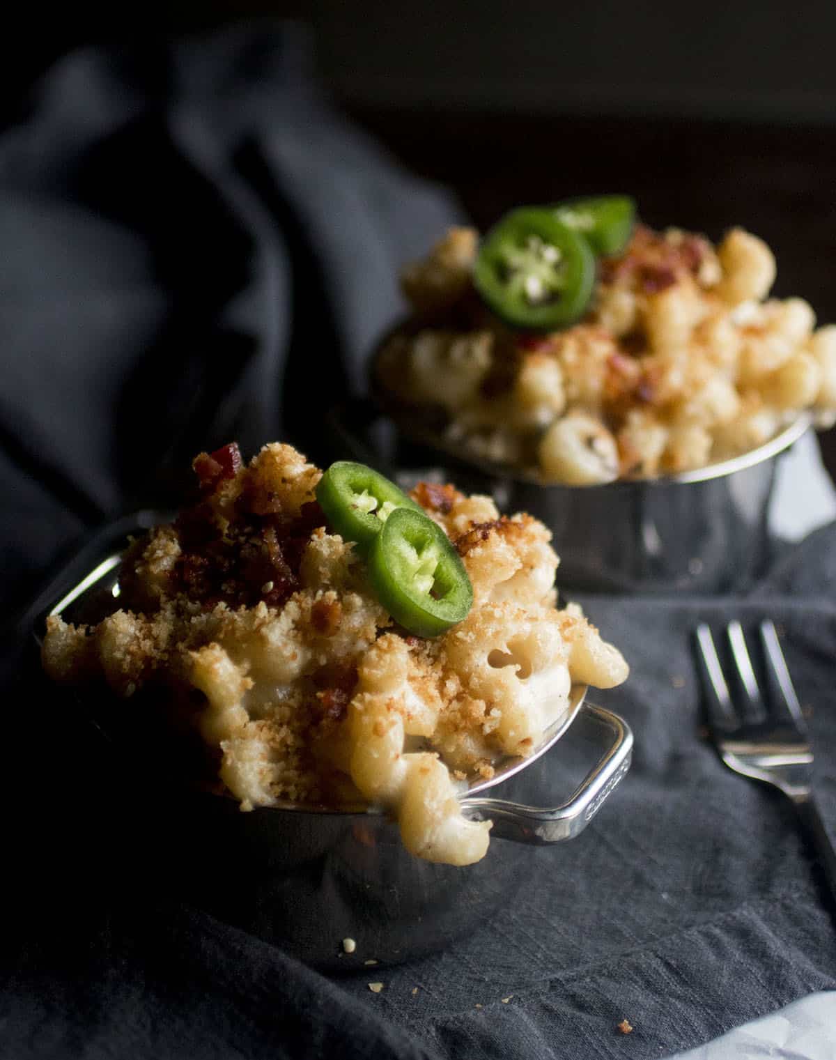 Two small ramekins, filled with mac and cheese and topped with bread crumbs.