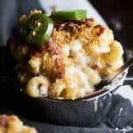 Mac and cheese in a silver baking dish, topped with bread crumbs, bacon, and sliced jalapeños.