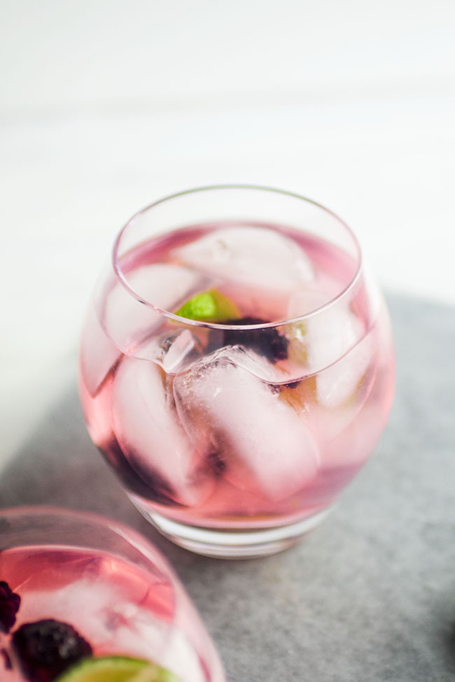 Glass cup filled with light pink cocktail and ice cubes on a white background.