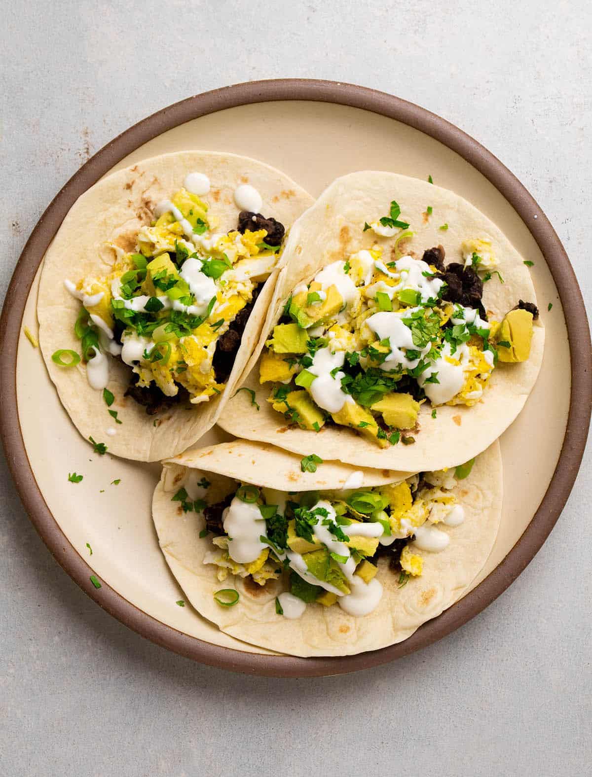 Three tacos with scrambled eggs on a large plate.