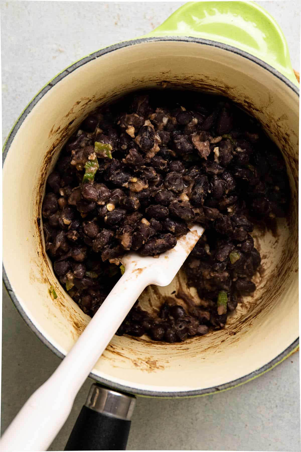 White spatula stirring cooked black beans in a small pot.