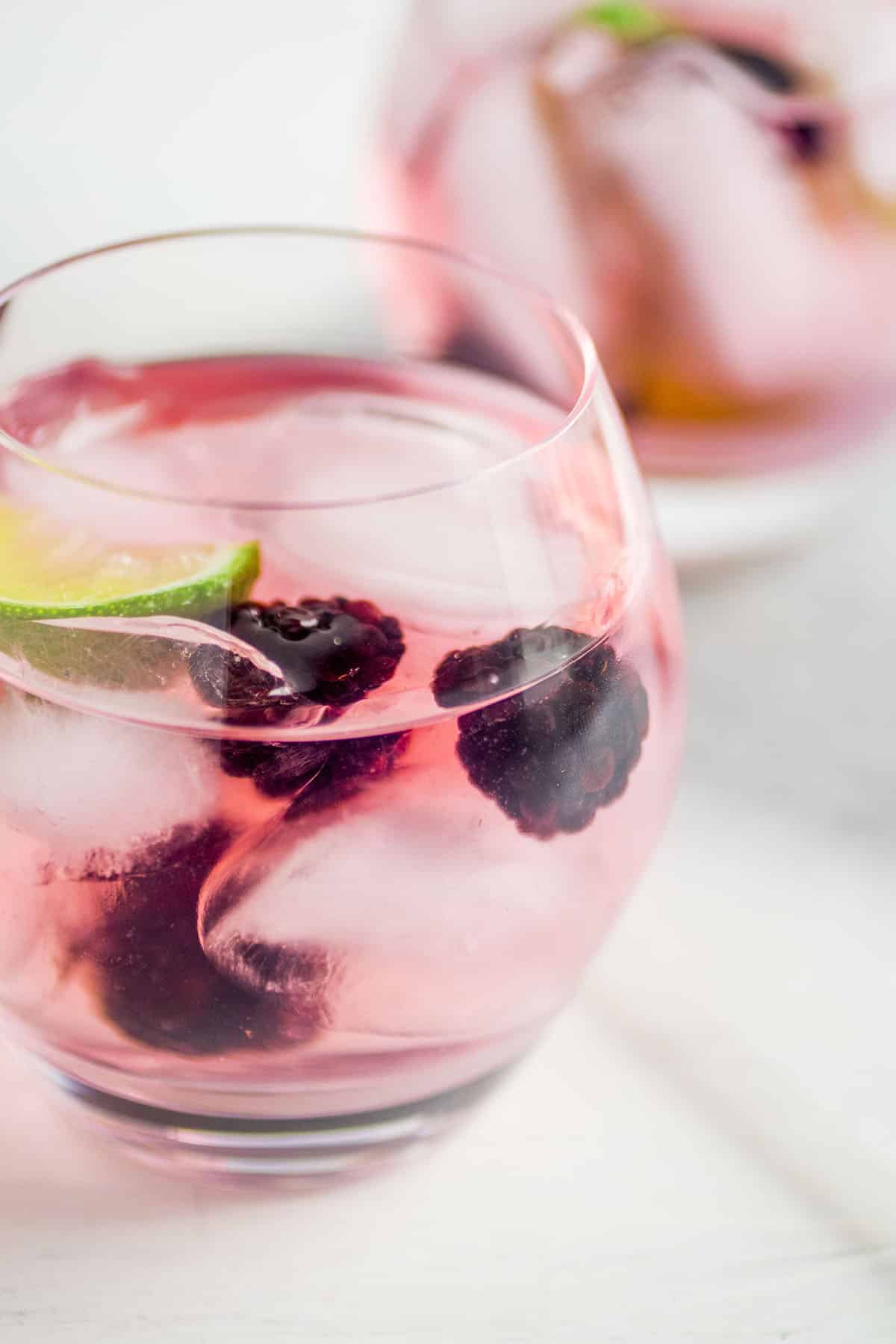 Blackberry vodka tonic in a short glass with a lime wedge.