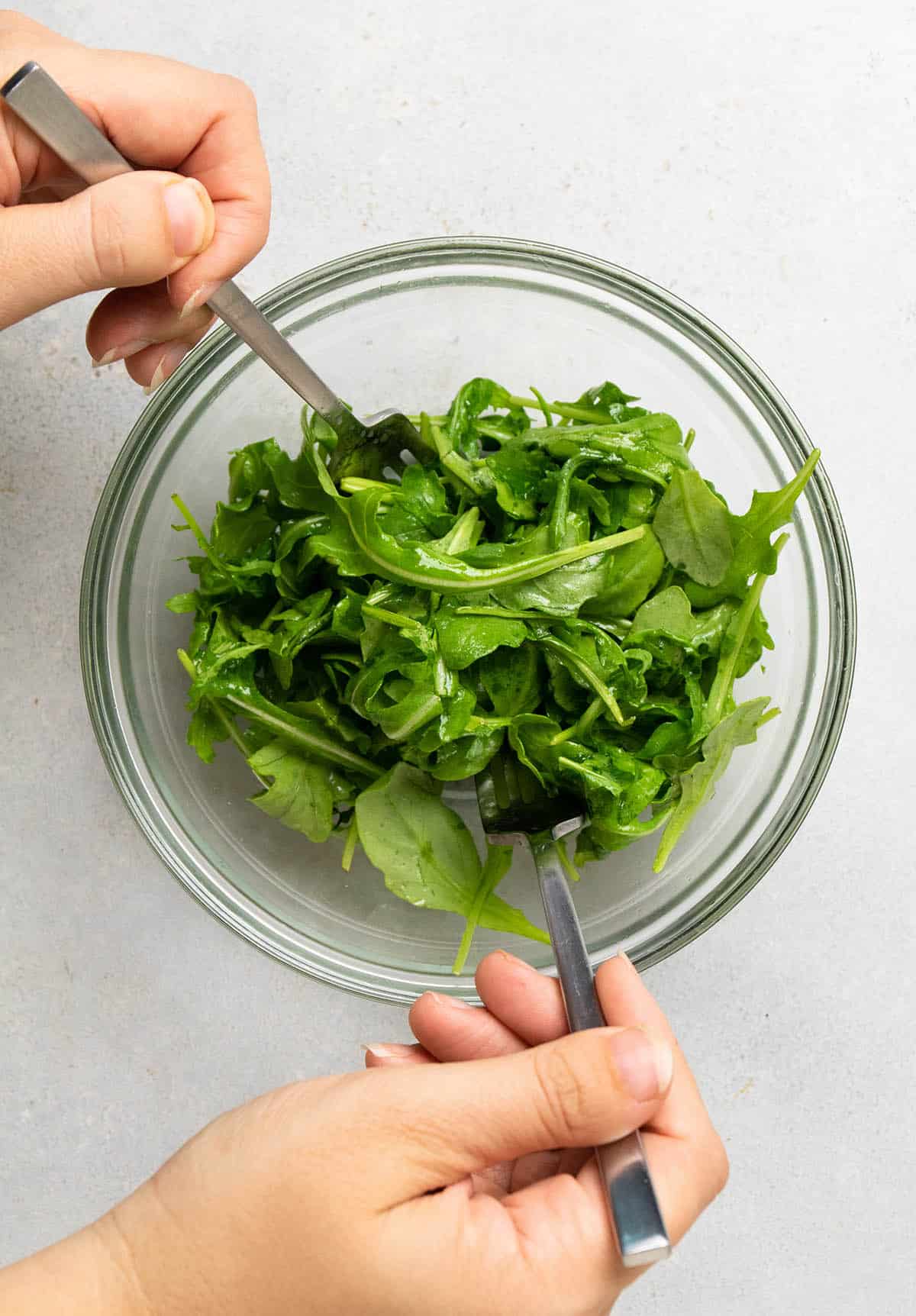 Two forks tossing fresh arugula with lemon juice and olive oil.