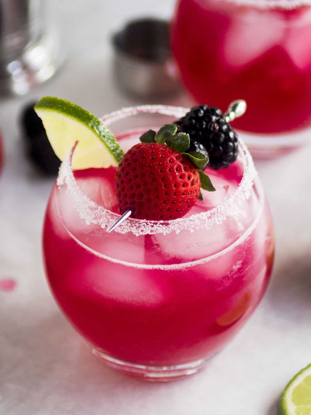 Berry margarita in a sugar-rimmed glass, topped with fresh berries on a skewer.