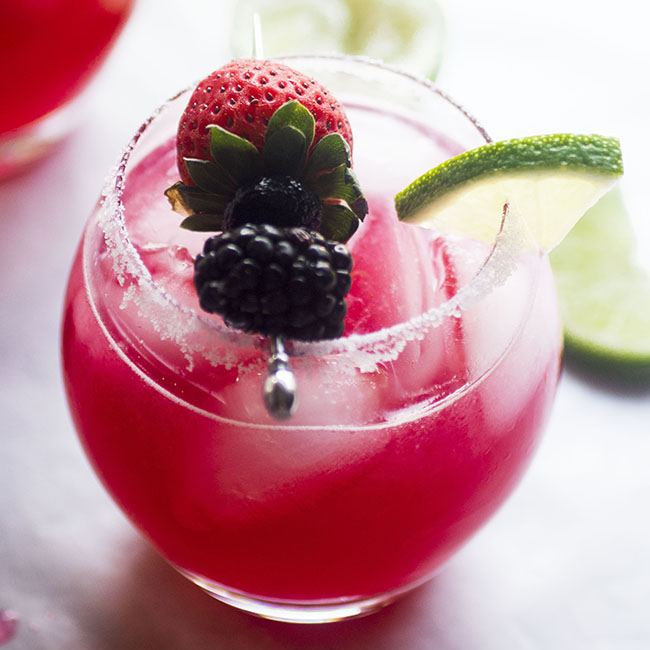 Margarita in a glass topped with fresh berries and a lime wedge.