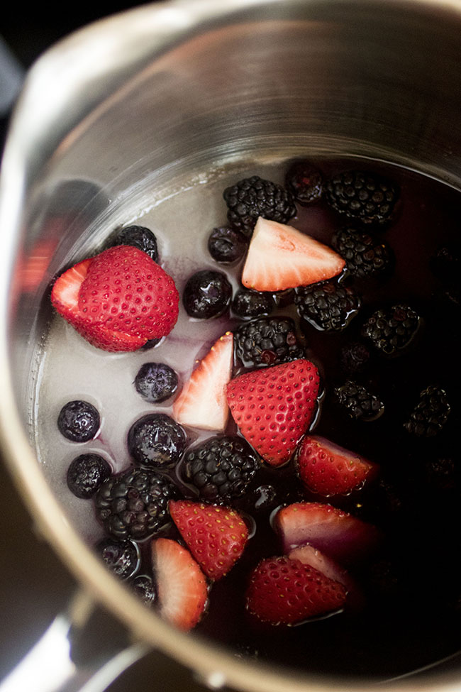 Strawberries, blueberries, and blackberries in a saucepan with water and sugar.
