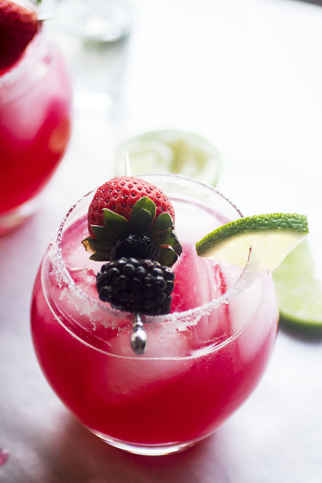 Cocktail cup filled with triple berry margaritas topped with a strawberry, blackberry, and slice of lime.