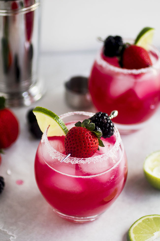 Berry margaritas with a salt rim, garnished with a metal toothpick filled with fresh berries.