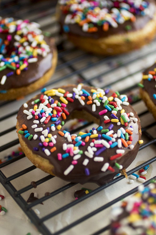 Chocolate glazed donuts with rainbow sprinkles on a wire cooling rack.