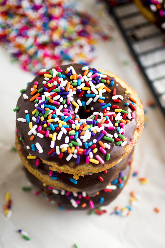 Three donuts with chocolate glaze and rainbow sprinkles stacked on top of each other.