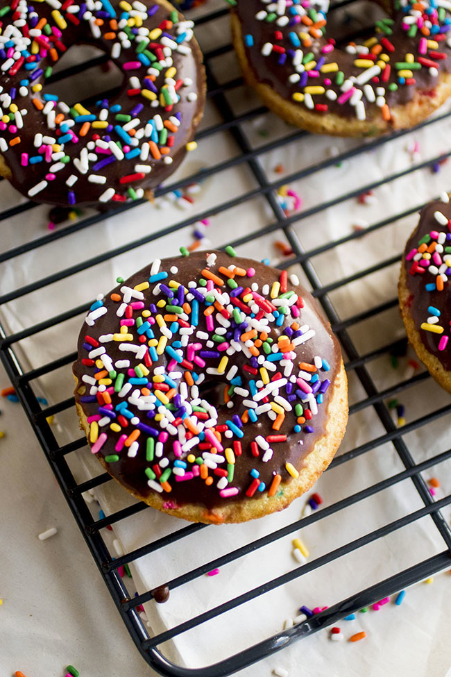 Funfetti donuts with chocolate glaze and rainbow sprinkles on a wire cooling rack.