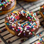 Chocolate glazed donut with rainbow sprinkles on a cooling rack.