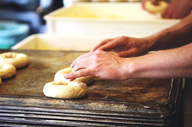 Hands forming bagels out of raw dough.