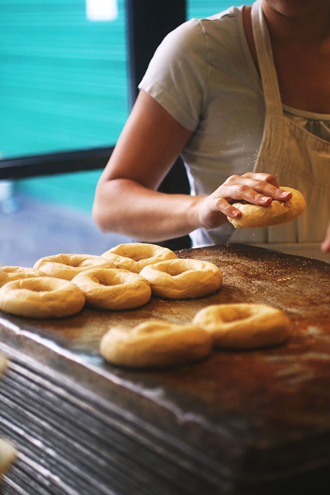 Woman placing formed bagel dough onto a large sheet pan.
