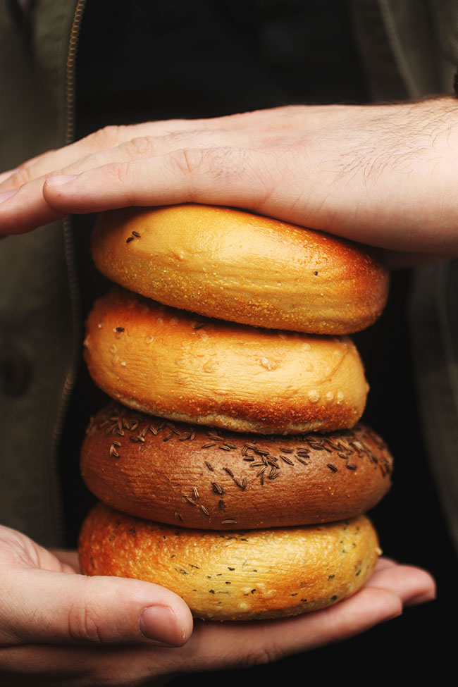 Hands holding a stack of four bagels.