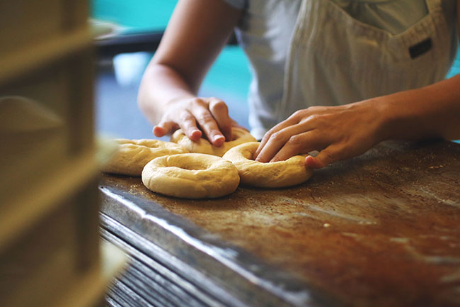 Woman shaping dough into a bagel shape.