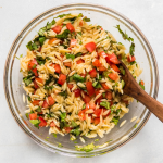 Glass bowl of orzo pasta salad with wooden spoon.