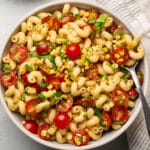 Corn and tomato pasta salad in a white bowl with a silver spoon.